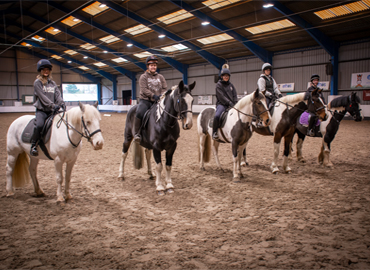 Five Equine students sat on horses in a line in the indoor arena