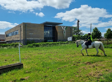 Photo of student riding a horse on the uncovered outdoor arena